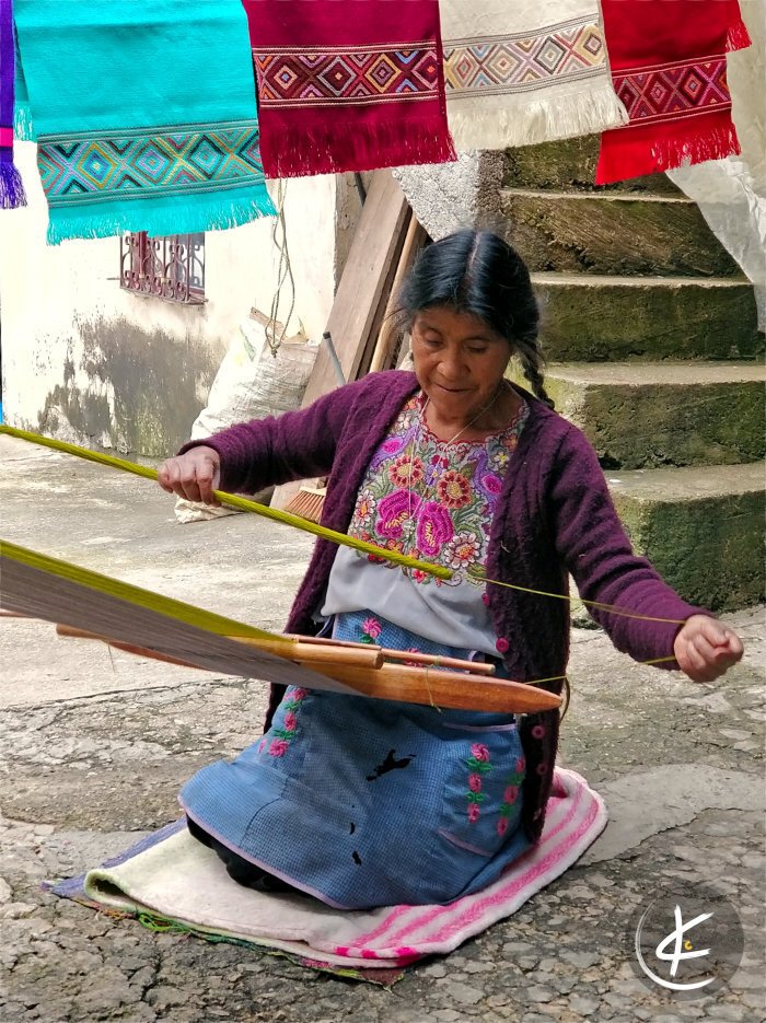 Indianerin hockt auf dem Boden und webt an einem Schal