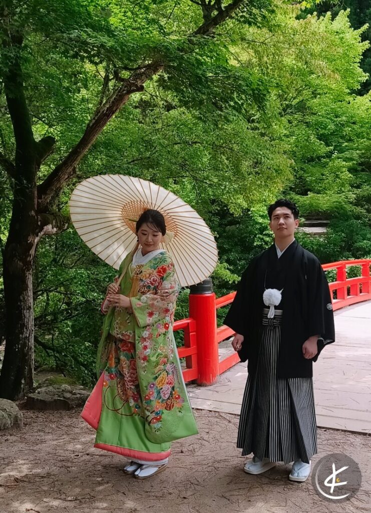 Japanisches Paar in traditionellen Kimonos steht im grünen an einer Brücke